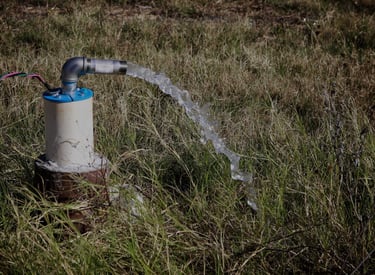 Electric submersible water well pump discharging a stream of clear water into a grassy field.