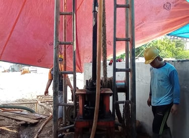 Construction workers operating a water well drilling rig at a construction site with red tarp.