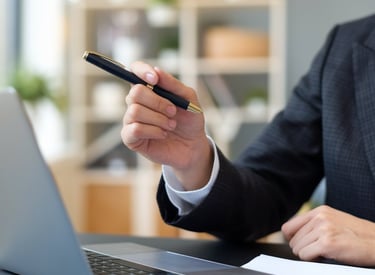 a man in a suit and tie is holding a pen and looking at a laptop