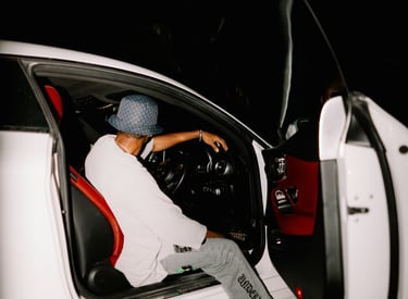 A person in streetwear sitting in a white luxury car with red leather interior at night.