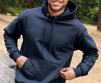 a man in a blue hoodie and jeans standing in front of a log cabin