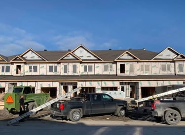 New multi-family townhouse construction project with house wrap, pickup trucks, and heavy equipment.