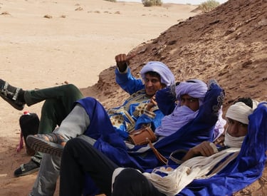 Three nomad guides in traditional dress lie down in a sand dune in the Moroccan Sahara desert