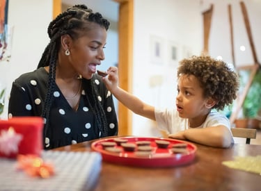 a black woman eating a snack from the hands of a black toddler with an afro