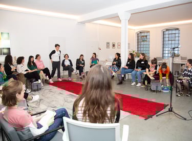 Workshop room, with red carpet in middle, women sitting around it, 1 woman walking down, towards mic