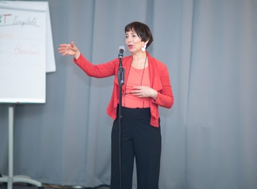Female public speaking coach, wearing red vest, talking behind microphone, explain with hand gesture