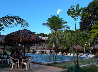 Centro Recreacional Mokanranko with thatched umbrellas, palm trees, and guests relaxing at the pool.