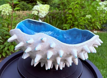 Handmade spiky ceramic bowl with white textured exterior and vibrant blue glazed interior in a garden.