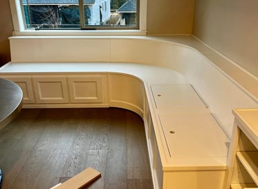 Custom white built-in corner banquet seating with integrated storage on dark wood floors.