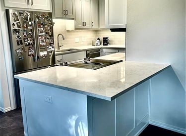 Modern white kitchen with marble countertops, stainless steel appliances, and shaker cabinets.