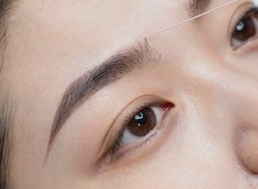 Close-up of a client receiving expert eyebrow shaping with tweezers in a cozy salon setting.