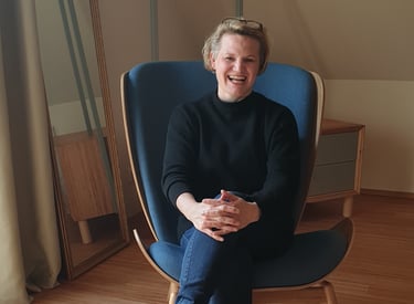 Sandra Schumacher sitzt in einem modernen blauen Ohrensessel in einem lichtdurchfluteten Raum.