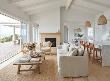 Modern coastal living room with white vaulted ceilings, marble kitchen island, and ocean view deck.