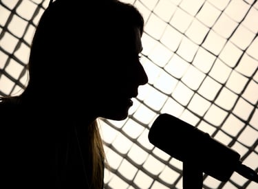 Silhouette of a female podcaster speaking into a microphone against a lit studio grid background.