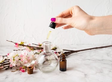 Hand using a glass dropper to put organic essential oil into a bottle near pink cherry blossoms.