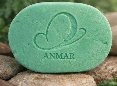 Anmar oval green natural soap bar with butterfly logo resting on river stones outdoors.