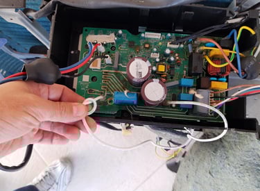 A technician repairing a damaged HVAC circuit board with capacitors and wiring components.