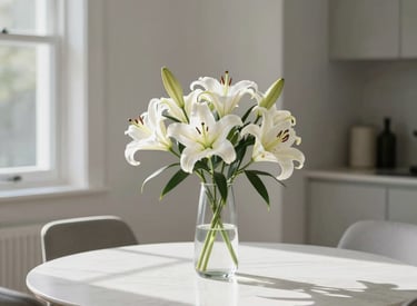 A clean, modern North American residential interior featuring a minimalist dining table with a single glass vase of white lilies, bright morning light.