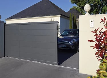 Automatic grey aluminum sliding gate opening to reveal a car parked in a modern home driveway.
