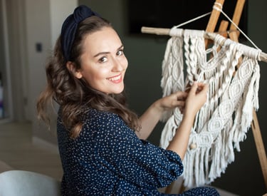 Mujer sonriente creando un tapiz de macramé blanco en casa.”