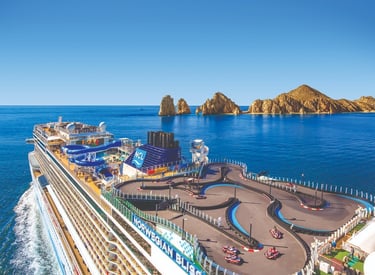 Norwegian Bliss cruise ship featuring a top-deck go-kart race track near coastal rock formations.