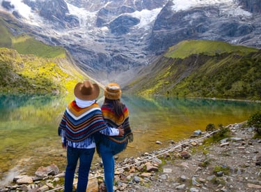 Couple in traditional ponchos overlooking Humantay Lake and snow-capped Andes mountains in Peru.