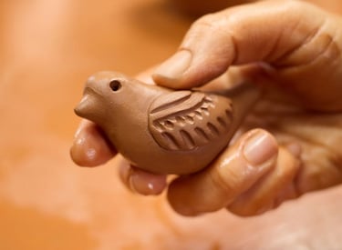 ceramista sosteniendo un pequeño silbato artesanal de barro marrón con tallados detallados.