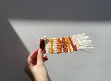 tapiz tejido, con texturas de hilo en tonos naranja, rojo y crema.