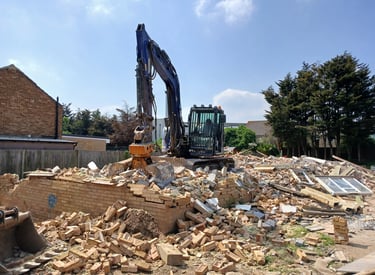 Heavy excavator clearing brick rubble and debris at a residential demolition site.
