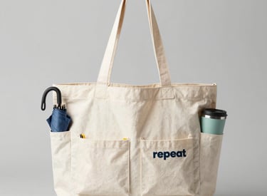 Black tote bags with minimalist prints, displayed hanging on hooks in a cozy setting.