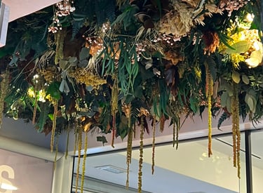 A lush indoor ceiling installation featuring a variety of dried flowers, ferns, and hanging green foliage.