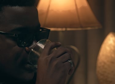 Cinematic frame from the short film Grief directed by Daniel da Trindade showing a man drinking in warm lamp light.