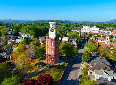 Aerial view of the historic brick Clock Tower in Rome, Georgia, surrounded by lush green trees and city streets.