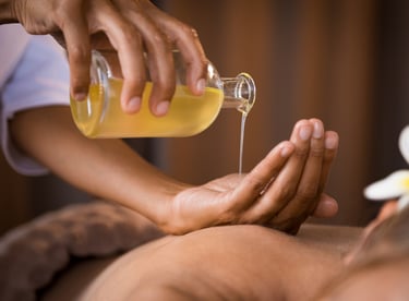 Thai aroma massage. A masseuse pores oil from into her hand above the bare back of a  lady