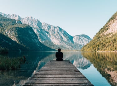 a person sitting on a dock with a mountain in the background