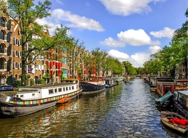 Scenic Amsterdam canal view with traditional houseboats and historic brick buildings under a blue sky.