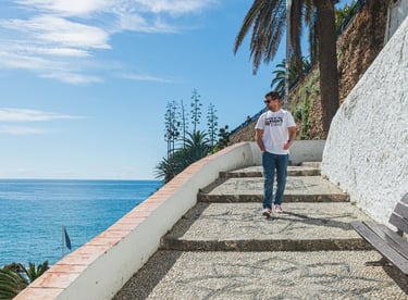 A man walks down scenic stone stairs overlooking the blue ocean and palm trees in Nerja, Spain.