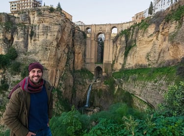 A man smiling in front of the historic Puente Nuevo bridge and El Tajo gorge in Ronda, Spain.