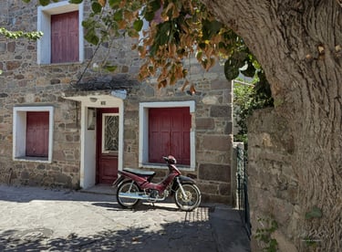 old burgundy moped in front of a stone house with burgundy shutters in Petra, Greece