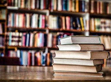 a stack of books on a table in front of a bookshelf