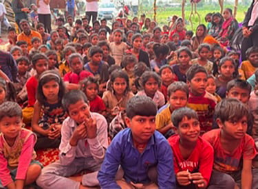 Group of around sixty children sitting on the ground celebrating Holi Festival.