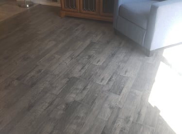 Modern dark gray wood-look luxury vinyl plank flooring installed in a living room with an armchair and media console.