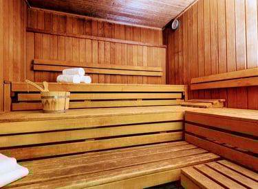 Modernes Sauna-Interieur aus Holz mit gestuften Bänken, Eimer, Schöpfkelle und weißen Handtüchern.
