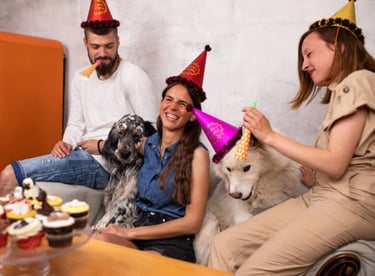Amigos con sombreros de fiesta celebran un cumpleaños con sus perros y pastelitos.