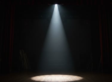 A single bright theater spotlight shining on an empty wooden stage with red curtains.