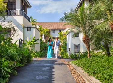 A couple walking down a tropical resort pathway lined with lush greenery, ferns, and palm trees