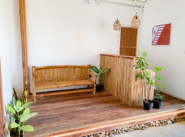 Rustic tropical bisita hostel reception bamboo furniture, wooden floors, and potted green plants.