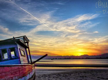 Barco encalhado na areia com entardecer ao fundo