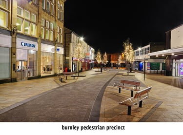 the pedestrian precinct of Burnley town centre at night, with buildings and benches and bushes