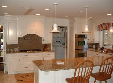 A spacious, brightly lit kitchen with white cabinets, granite countertops, stainless steel appliances, and a central island